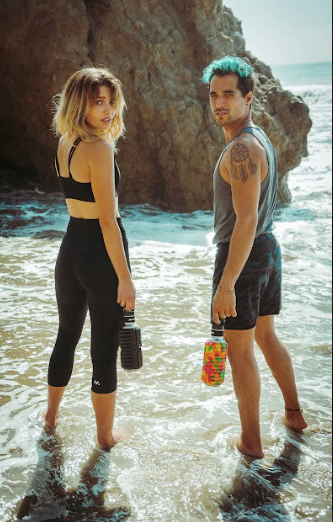 tattooed blue hair man and blond woman standing in the ocean holding Mobot foam roller water bottle  
