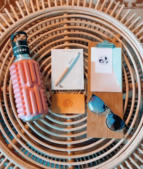 blush pink Mobot foam roller water bottle on a table with sunglasses and papers and pen
